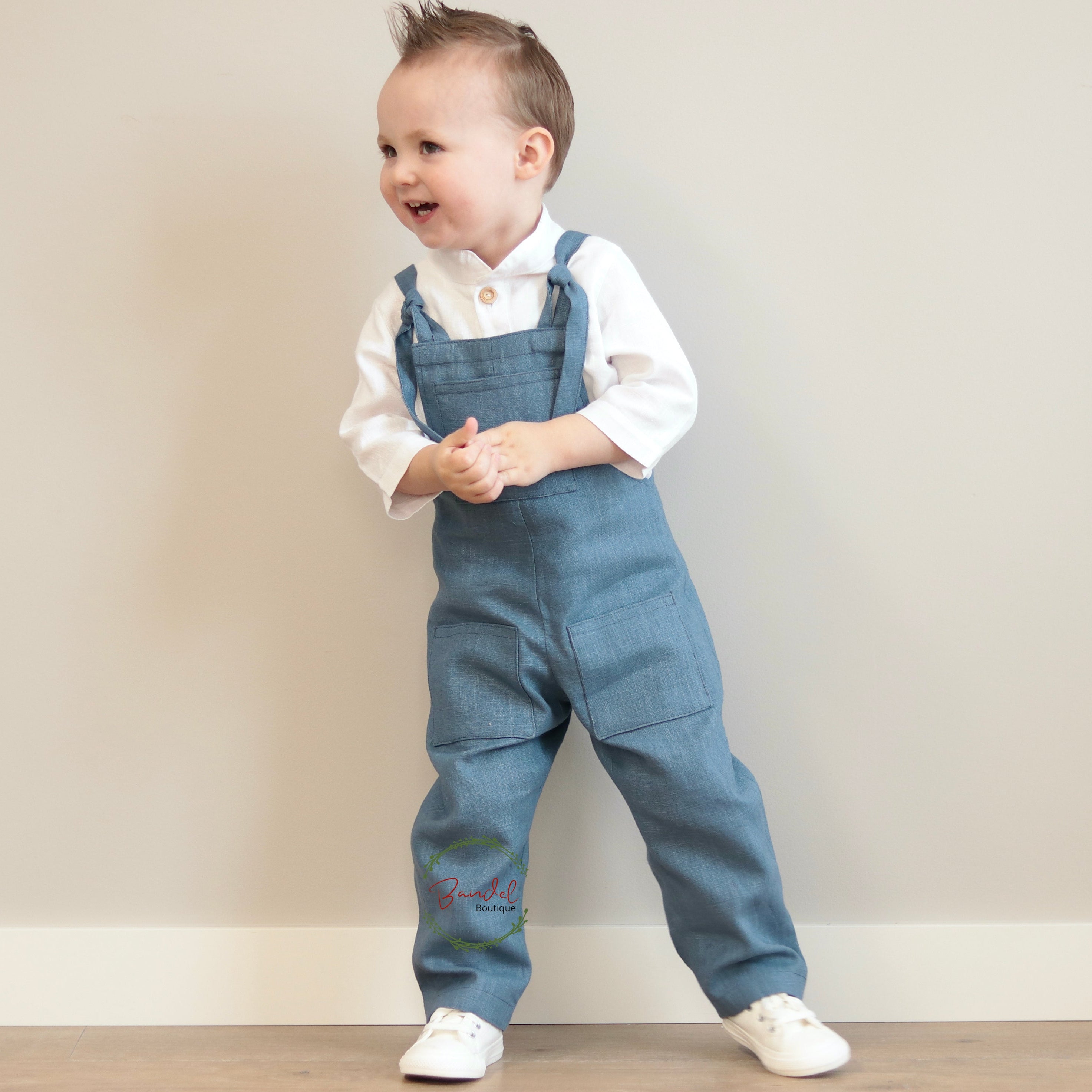 Child wearing blue denim overalls with a white shirt against a plain background