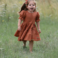 Linen Rust Dress is the perfect special-occasion look for your little flower girl. Made of breathable linen and featuring a square neckline, flutter sleeves, and a playful ruffle hem, this design is both comfortable and fashionable. The back of the dress has a double row of rustic wooden buttons for an elegant finishing touch.
