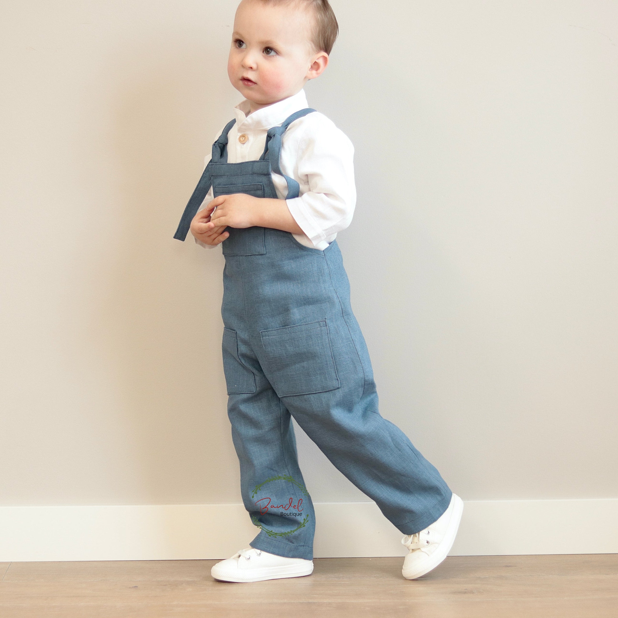 Child wearing blue denim overalls with a white shirt against a plain background