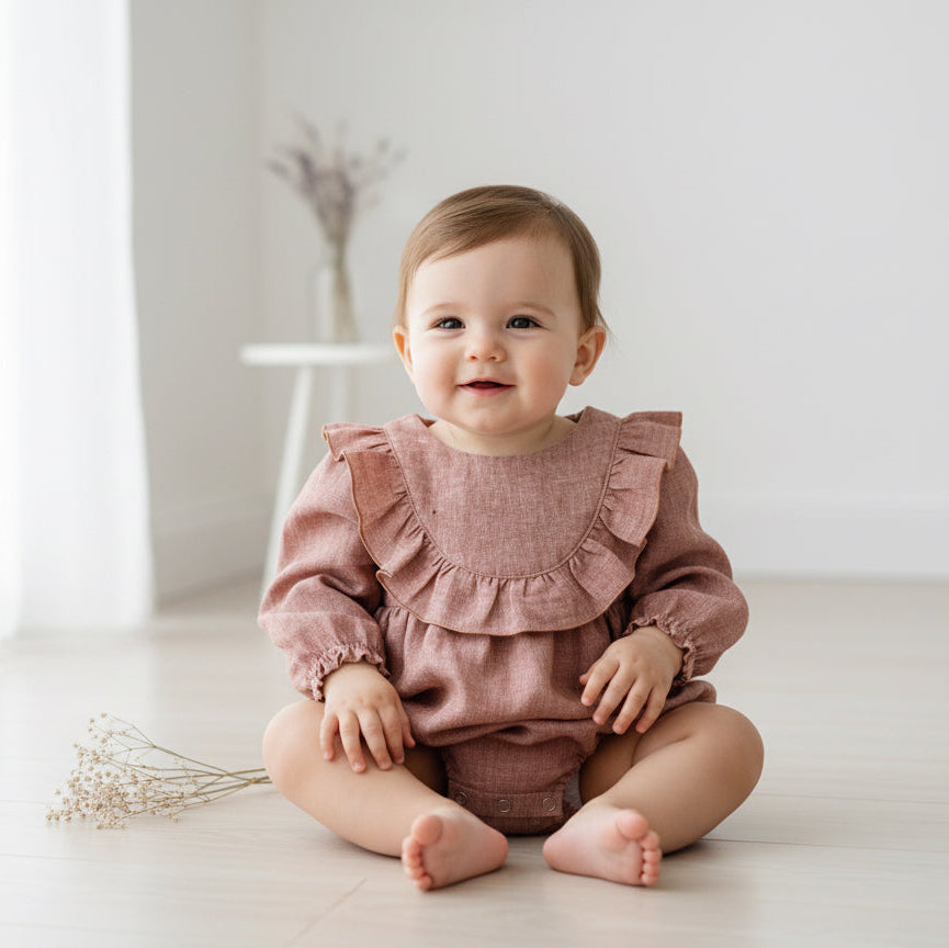 Baby wearing a brown ruffled outfit sitting on a white floor.
