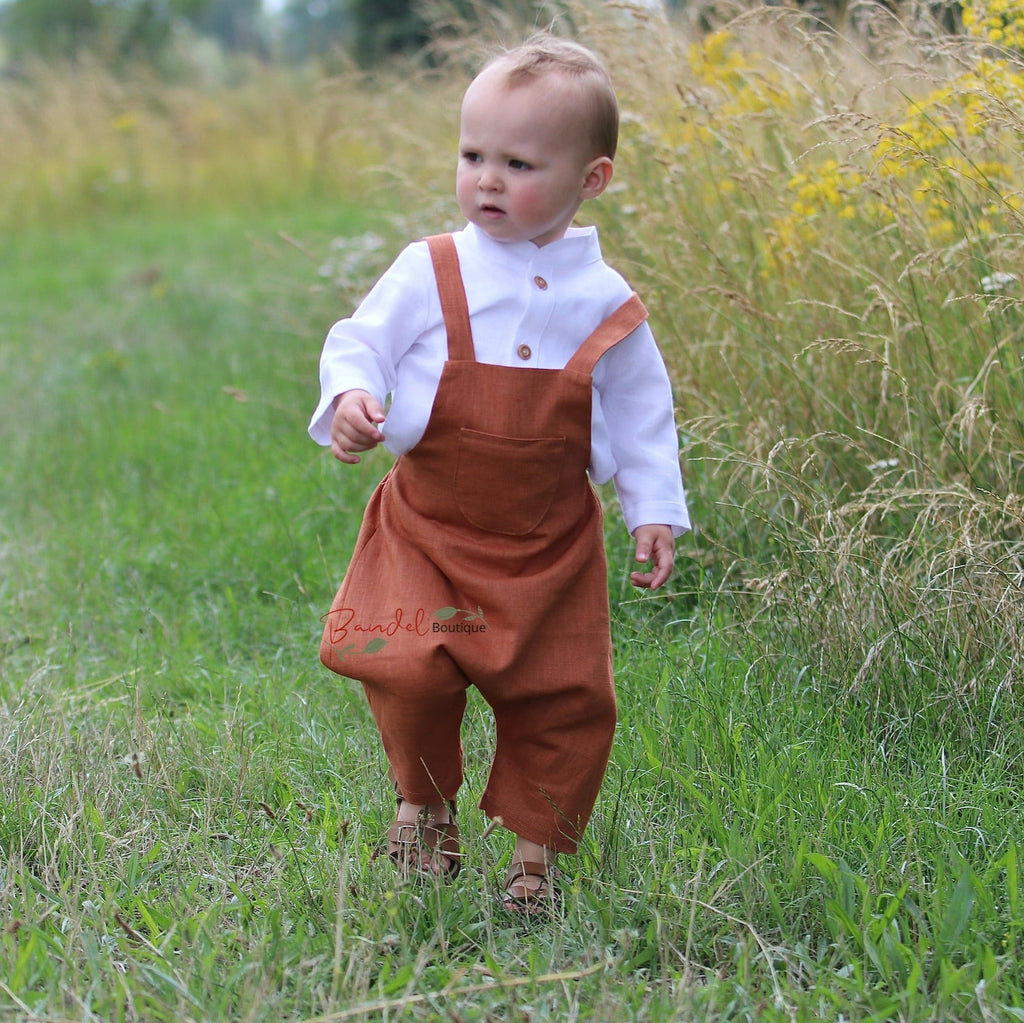 Rust Linen baby romper dungarees feature 3/4 length shorts with a traditional curved front pocket. The elastic back waistband and adjustable tie straps provide a secure fit, and the wooden button closure at the back creates a stylish look.