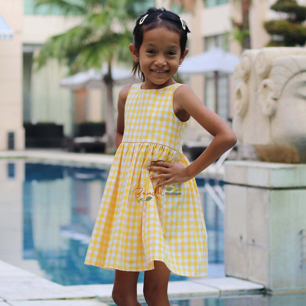 Young girl in a yellow dress standing by a poolside with a statue in the background