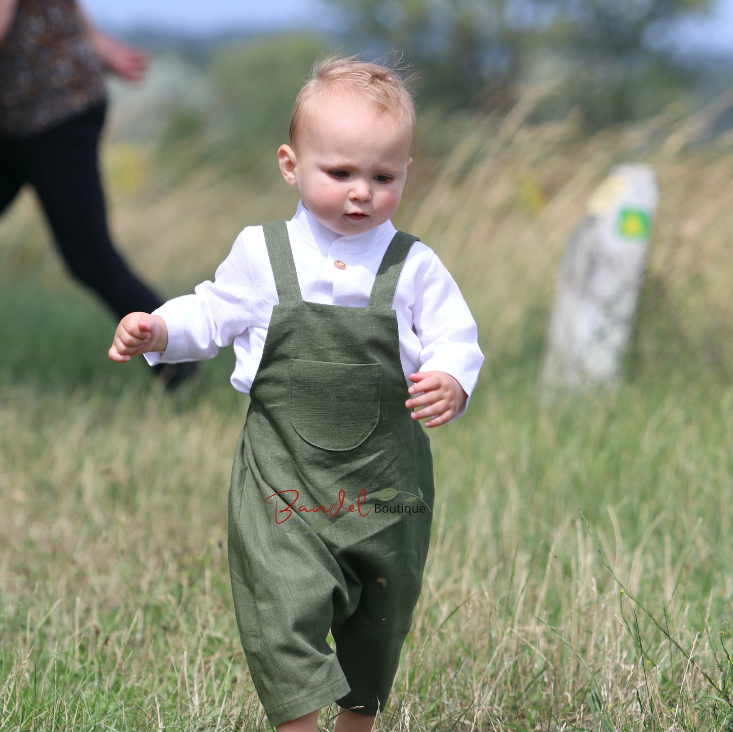 Child wearing green overalls and a white shirt in a grassy field