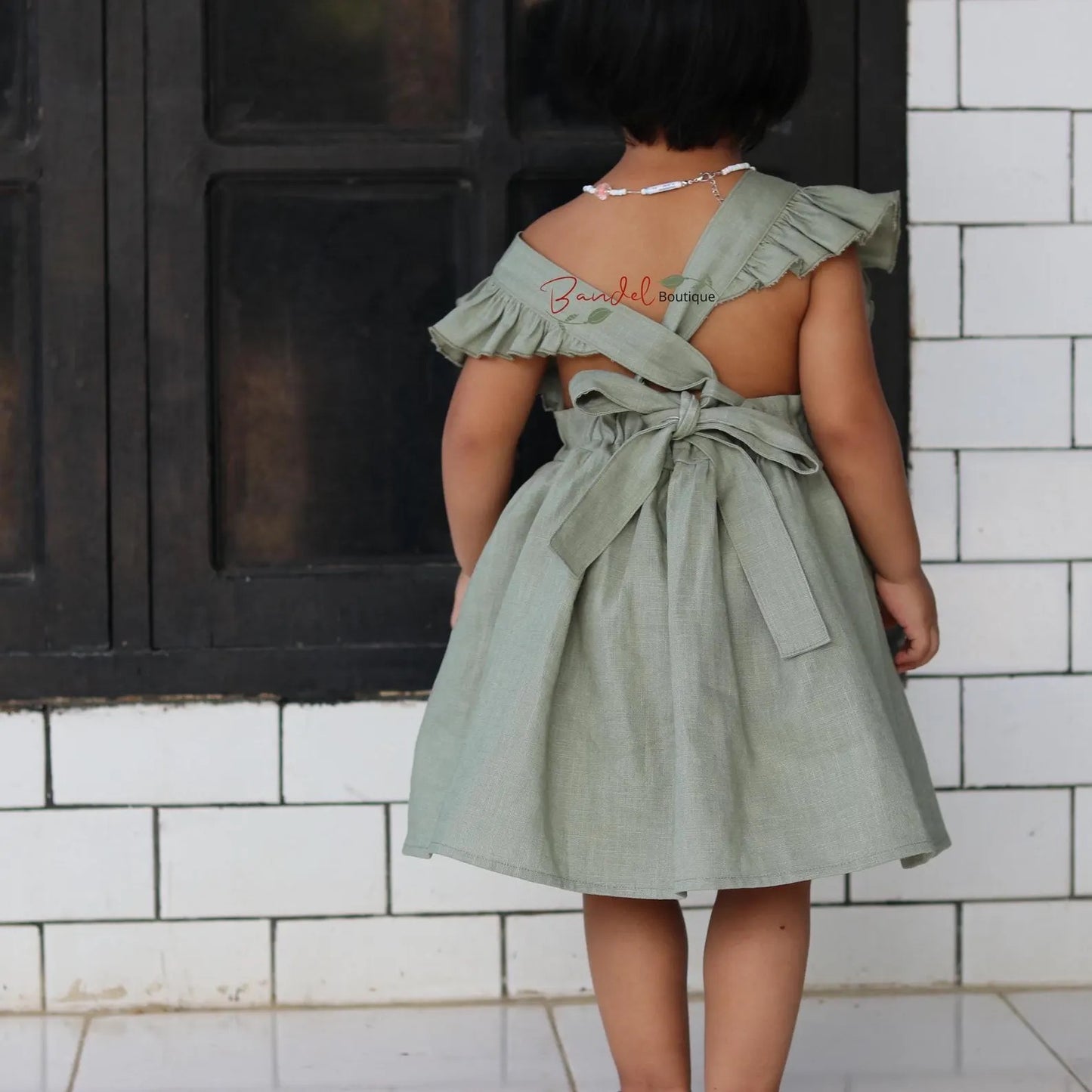 Person wearing a green dress with ruffled straps in front of a tiled wall.