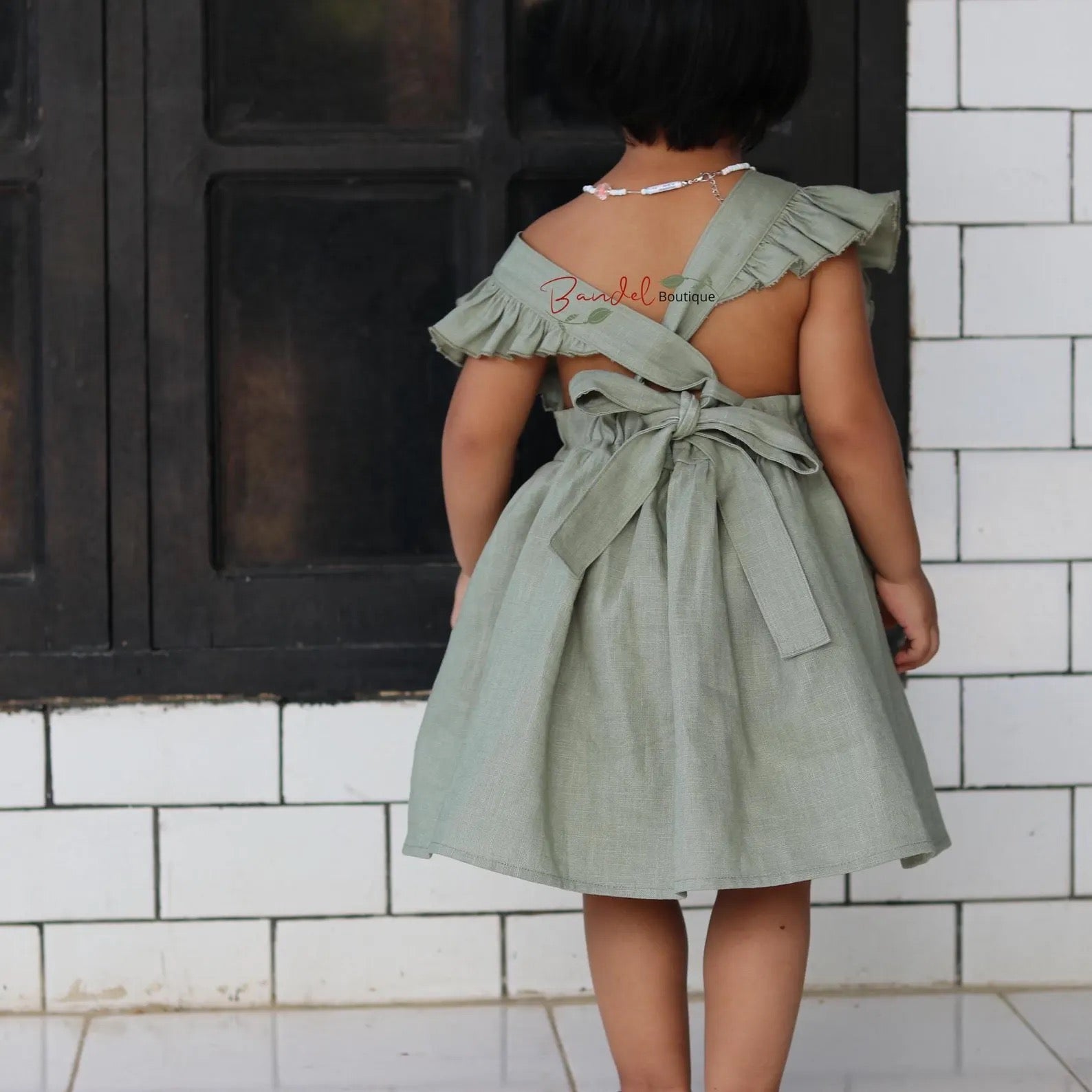 Person wearing a green dress with ruffled straps in front of a tiled wall.