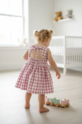 Child in a pink checkered dress standing in a bright room with toys.