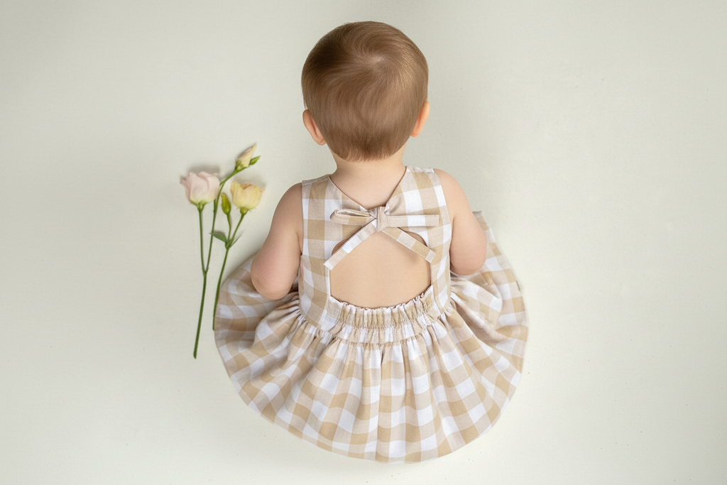 Child wearing a checkered dress with a bow detail, holding flowers against a plain background