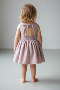 Child wearing a pink dress with a bow detail on a plain background