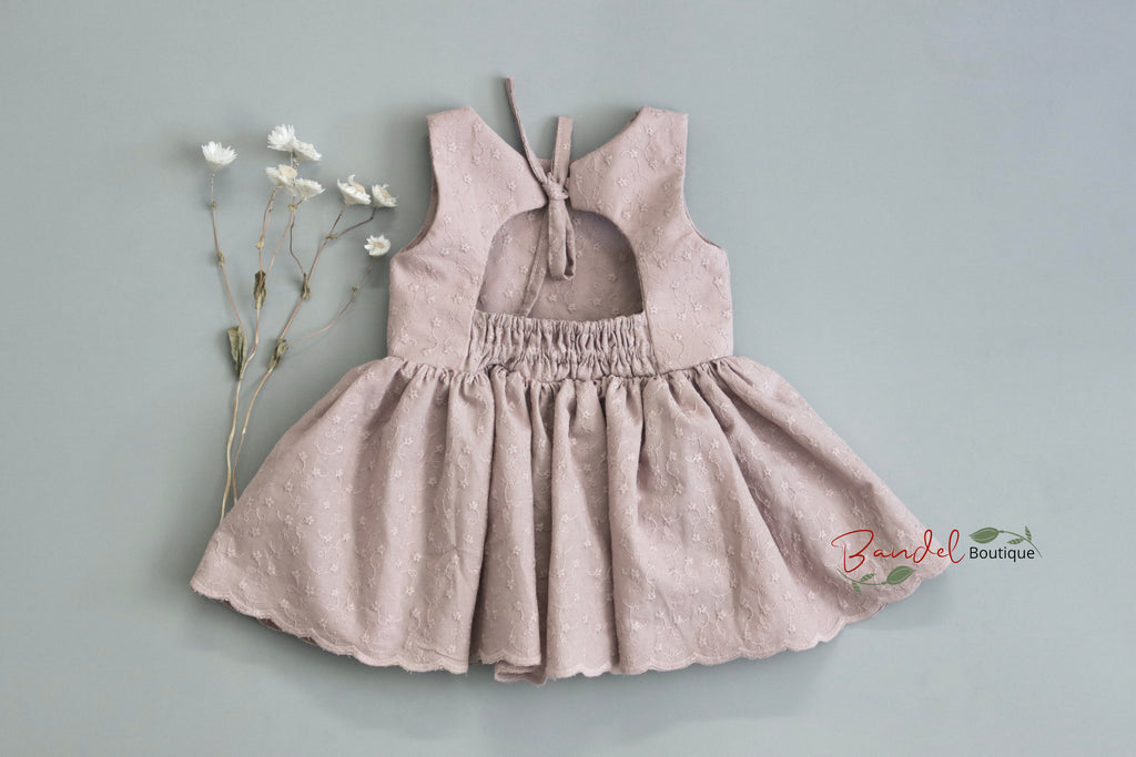 Young girl wearing a pink dress with a bow detail on a gray background