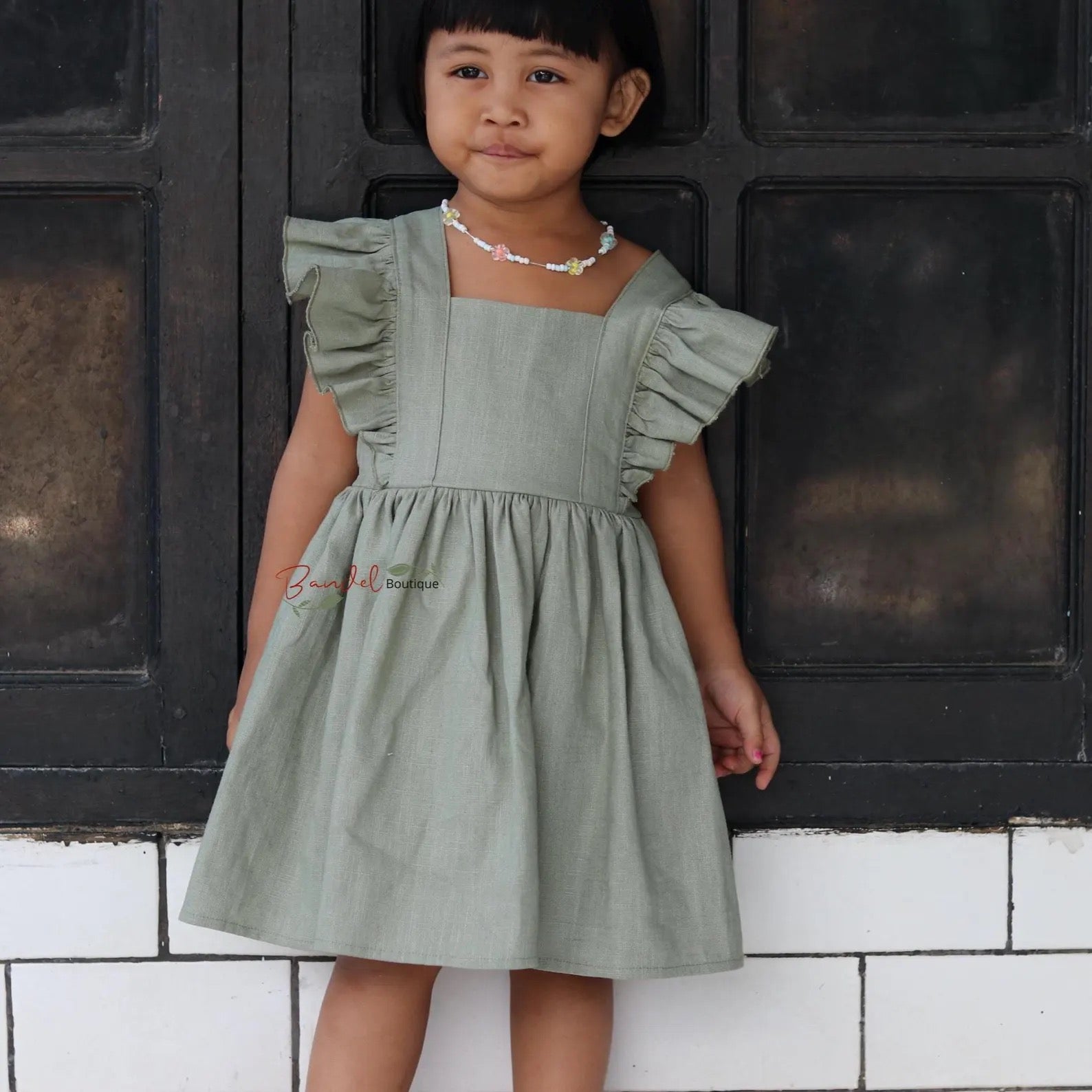Young girl wearing a green dress standing against a black and white tiled wall.