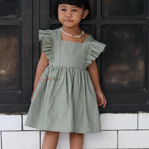 Young girl wearing a green dress standing against a black and white tiled wall.
