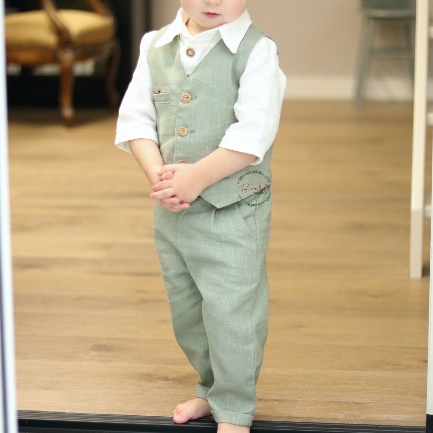 Child wearing a green vest and pants standing in front of a glass door.