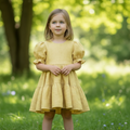 Young girl in a yellow dress standing in a grassy field with trees in the background