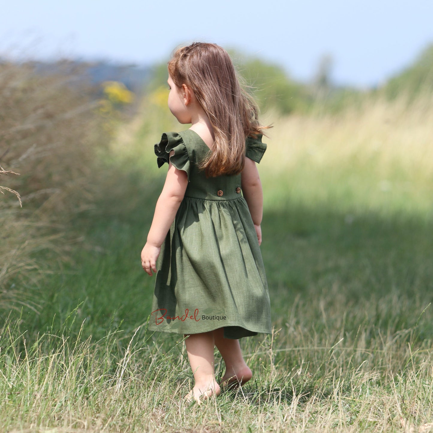 Child in a green dress standing in a grassy field with a blurred background