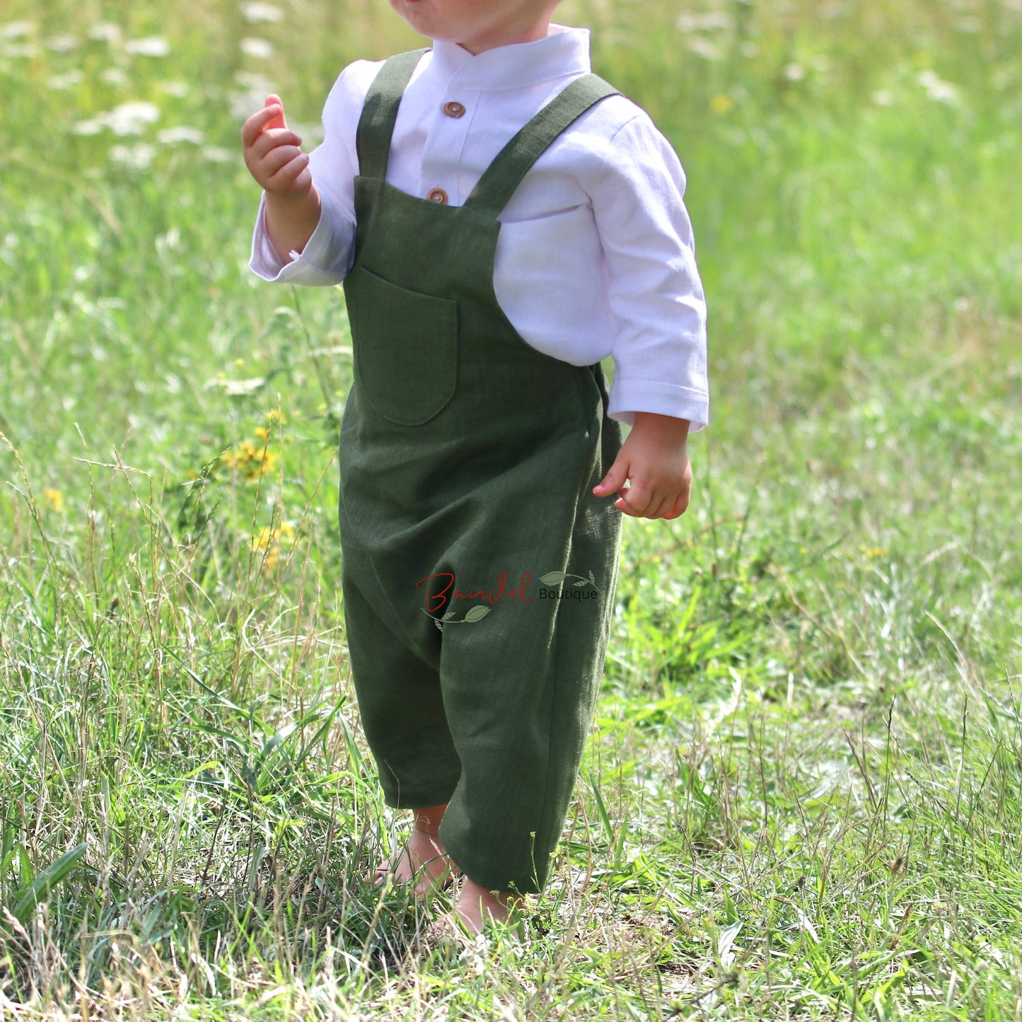 Child wearing green overalls and a white shirt in a grassy field
