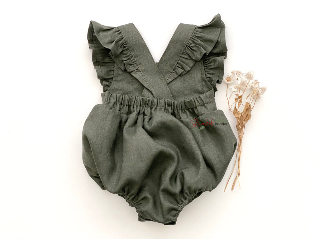 Baby wearing a green romper with ruffled straps on a white background