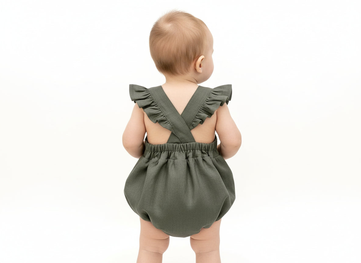 Baby wearing a green romper with ruffled straps on a white background