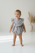 Baby wearing a gray romper with ruffled details against a white background