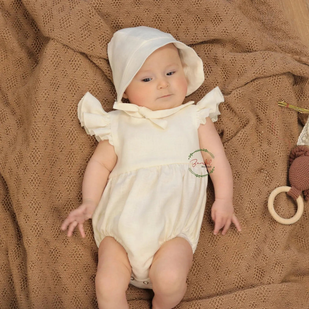 Baby in a white outfit and bonnet lying on a brown textured blanket.