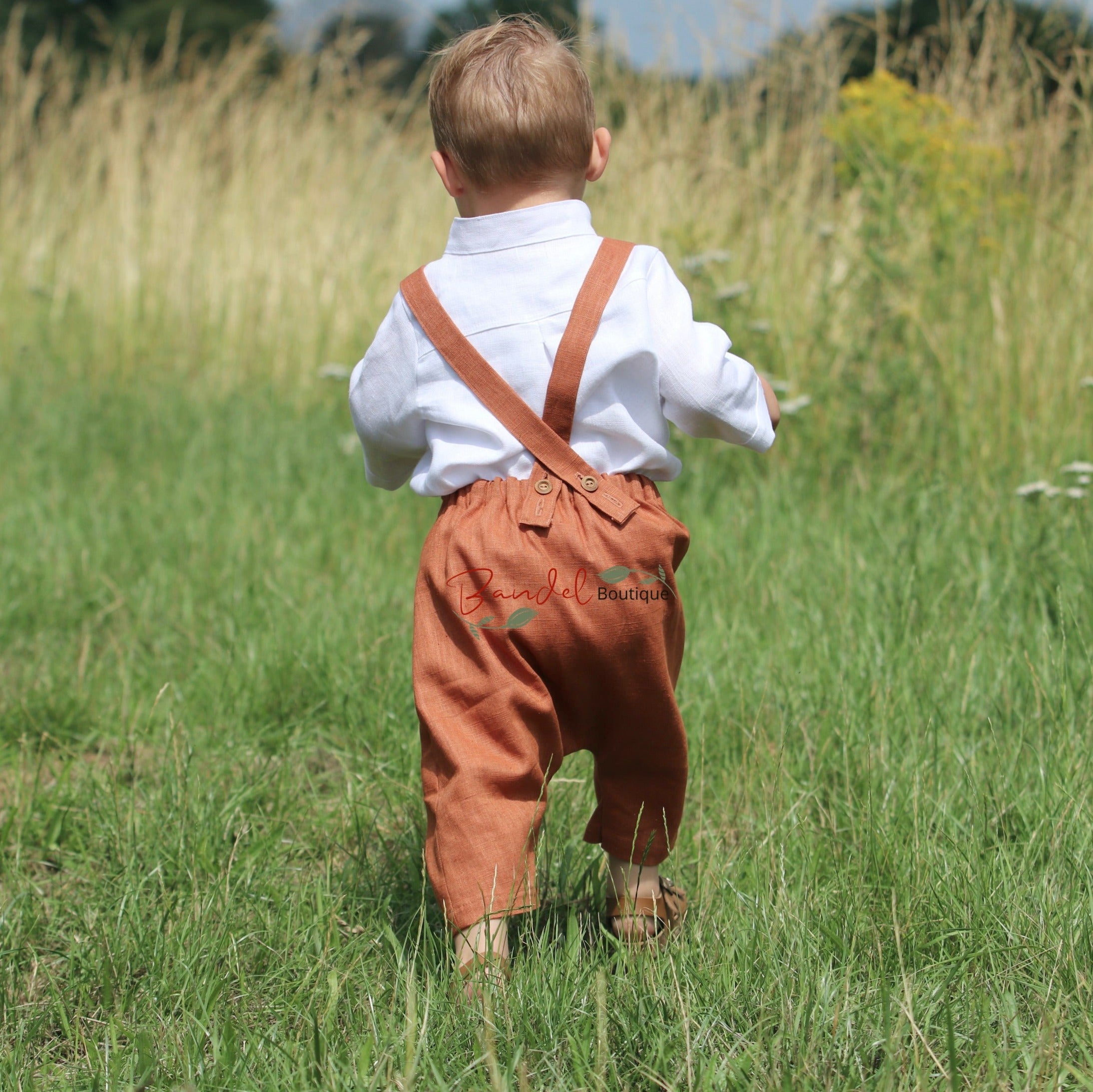 Rust Linen baby romper dungarees feature 3/4 length shorts with a traditional curved front pocket. The elastic back waistband and adjustable tie straps provide a secure fit, and the wooden button closure at the back creates a stylish look.