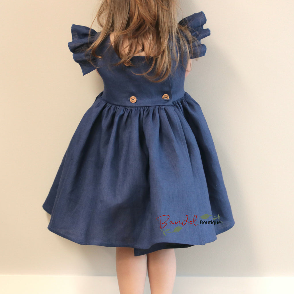 Child wearing a blue dress with ruffled sleeves against a beige background