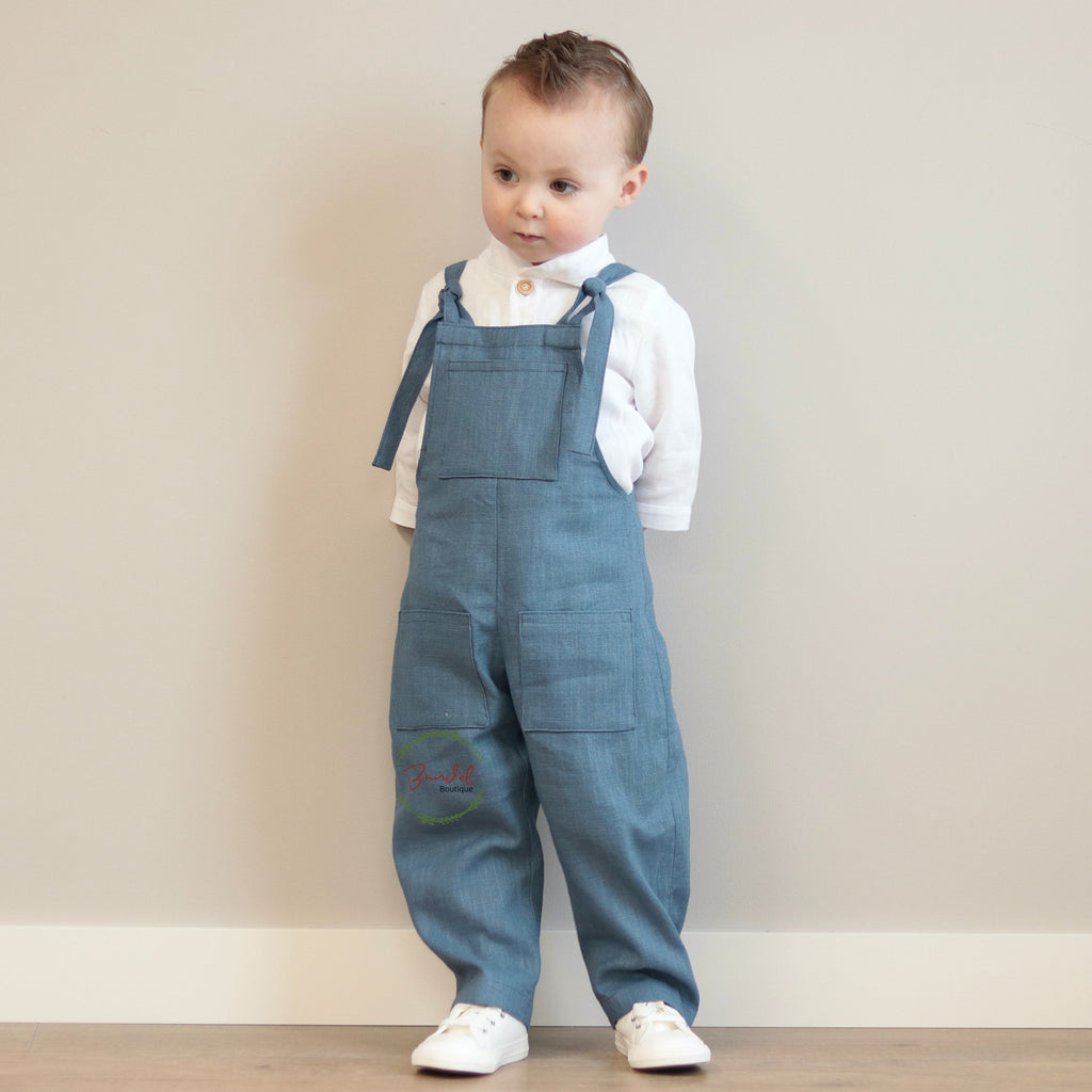 Child wearing blue denim overalls and a white shirt against a plain background