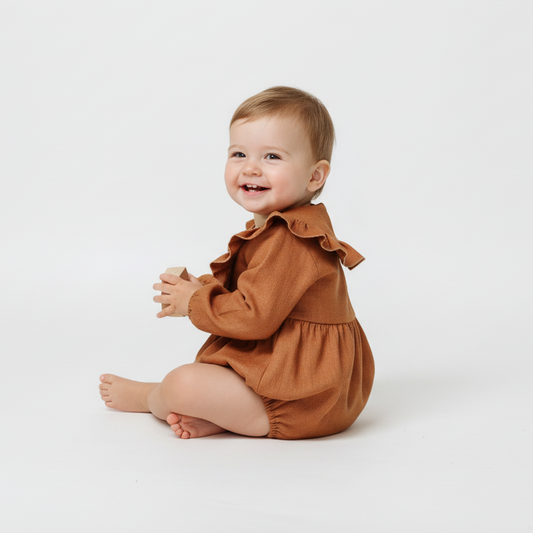 Baby wearing a brown romper sitting on a white background