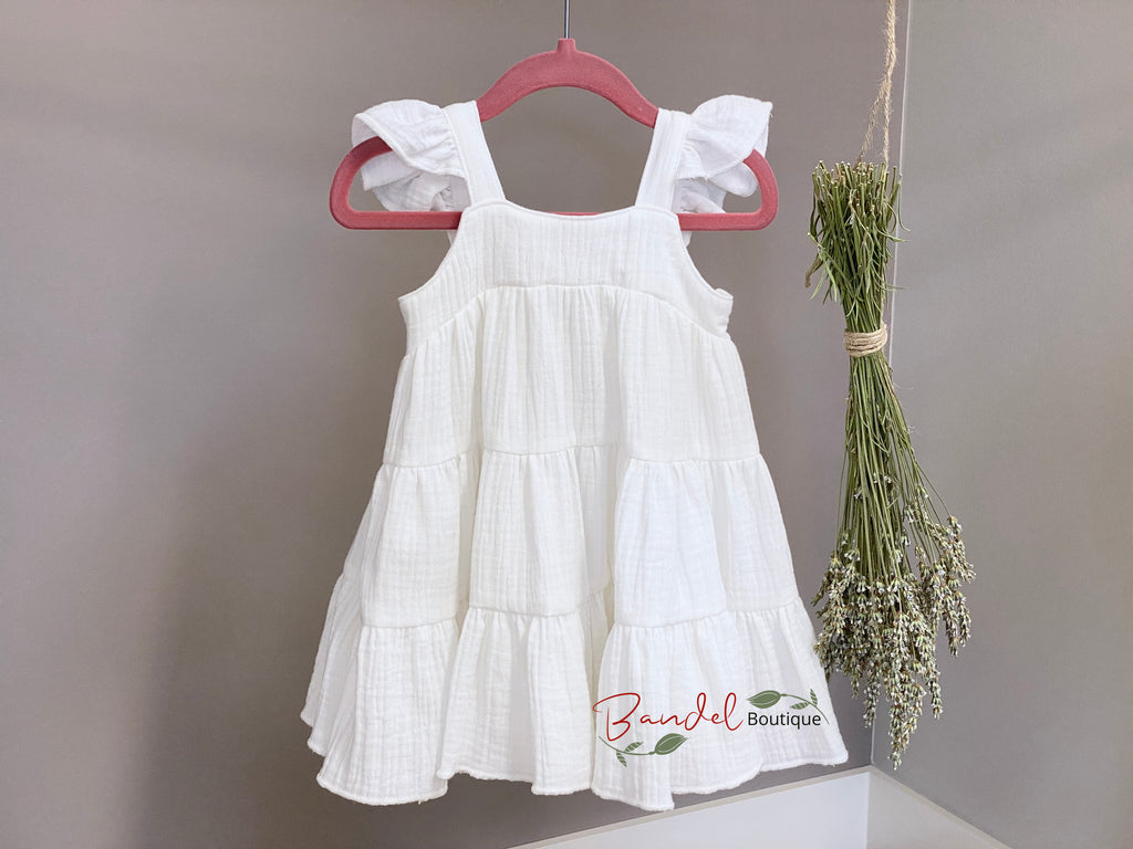 White dress with ruffled sleeves and bottom hanging on a pink hanger against a gray background.
