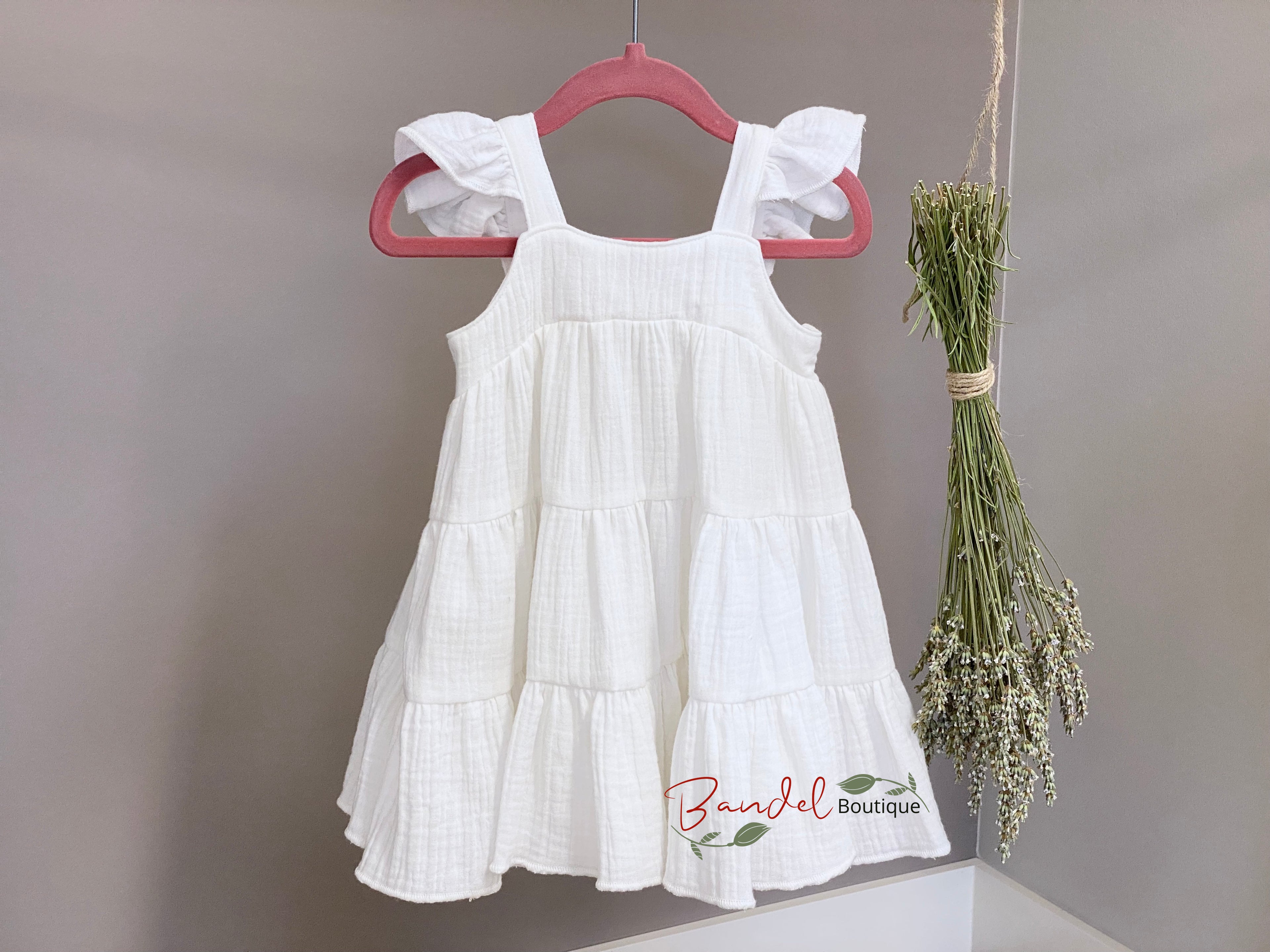 White dress with ruffled sleeves and bottom hanging on a pink hanger against a gray background.