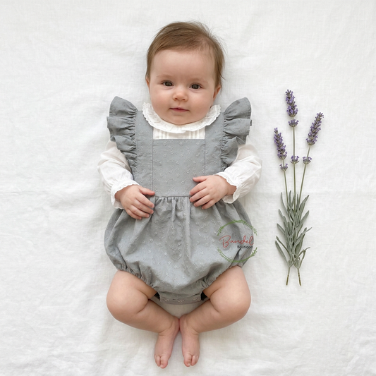 A baby lying on a white fabric background wearing a gray bubble romper over a white long-sleeve shirt, with lavender sprigs placed to the right. A small 'Breeze' brand watermark is visible on the romper.