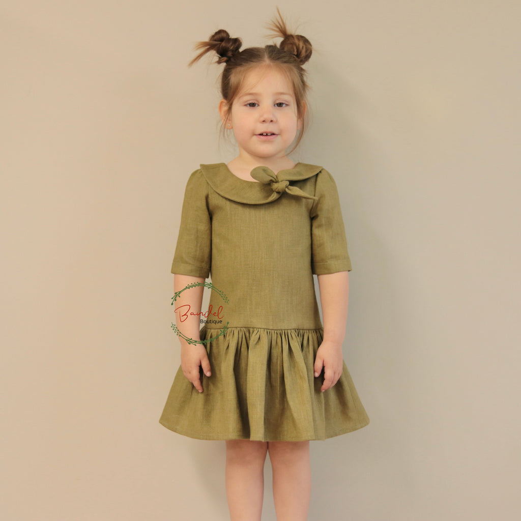 Young girl wearing a green dress with a bow collar against a beige background