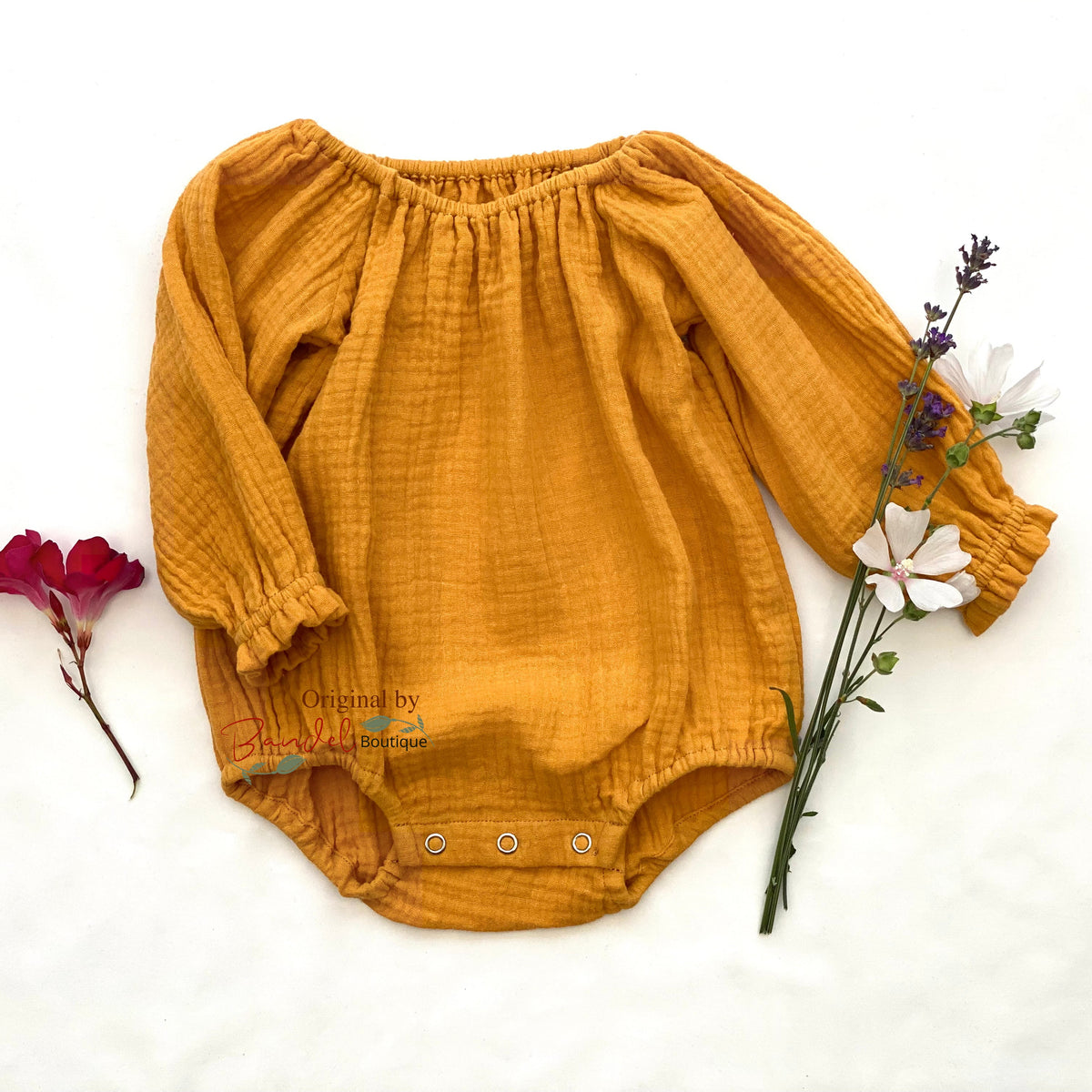 A mustard yellow gauze long-sleeve baby bodysuit laid flat on a white background, styled with small flowers on either side.