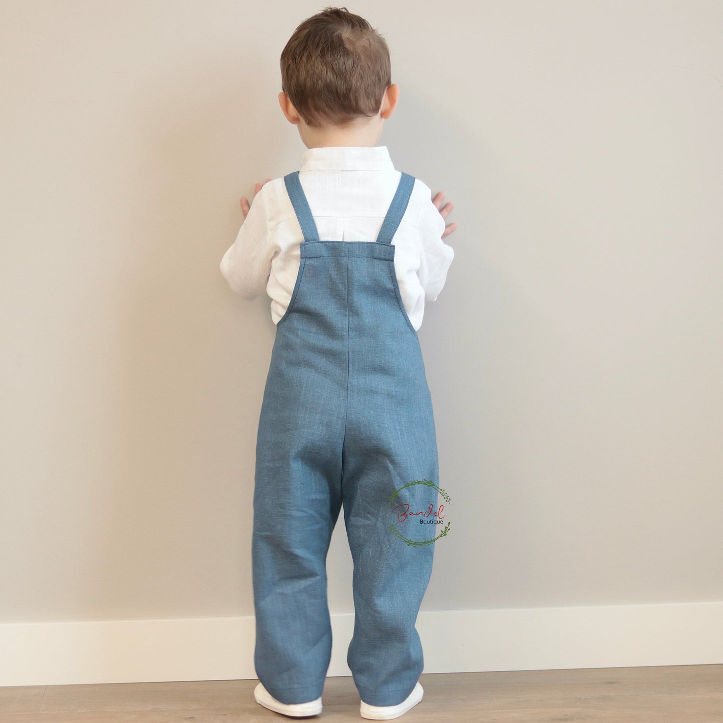 Child wearing blue denim overalls and a white shirt against a plain background