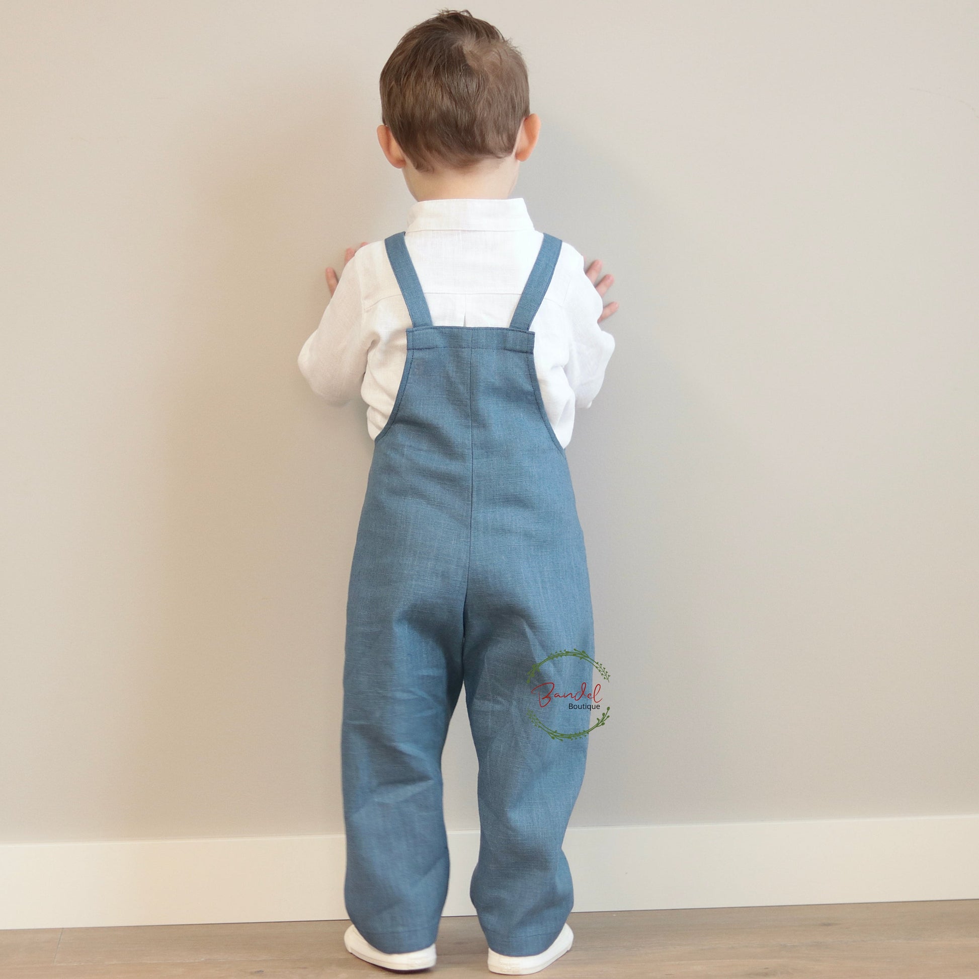 Child wearing blue denim overalls and a white shirt against a plain background