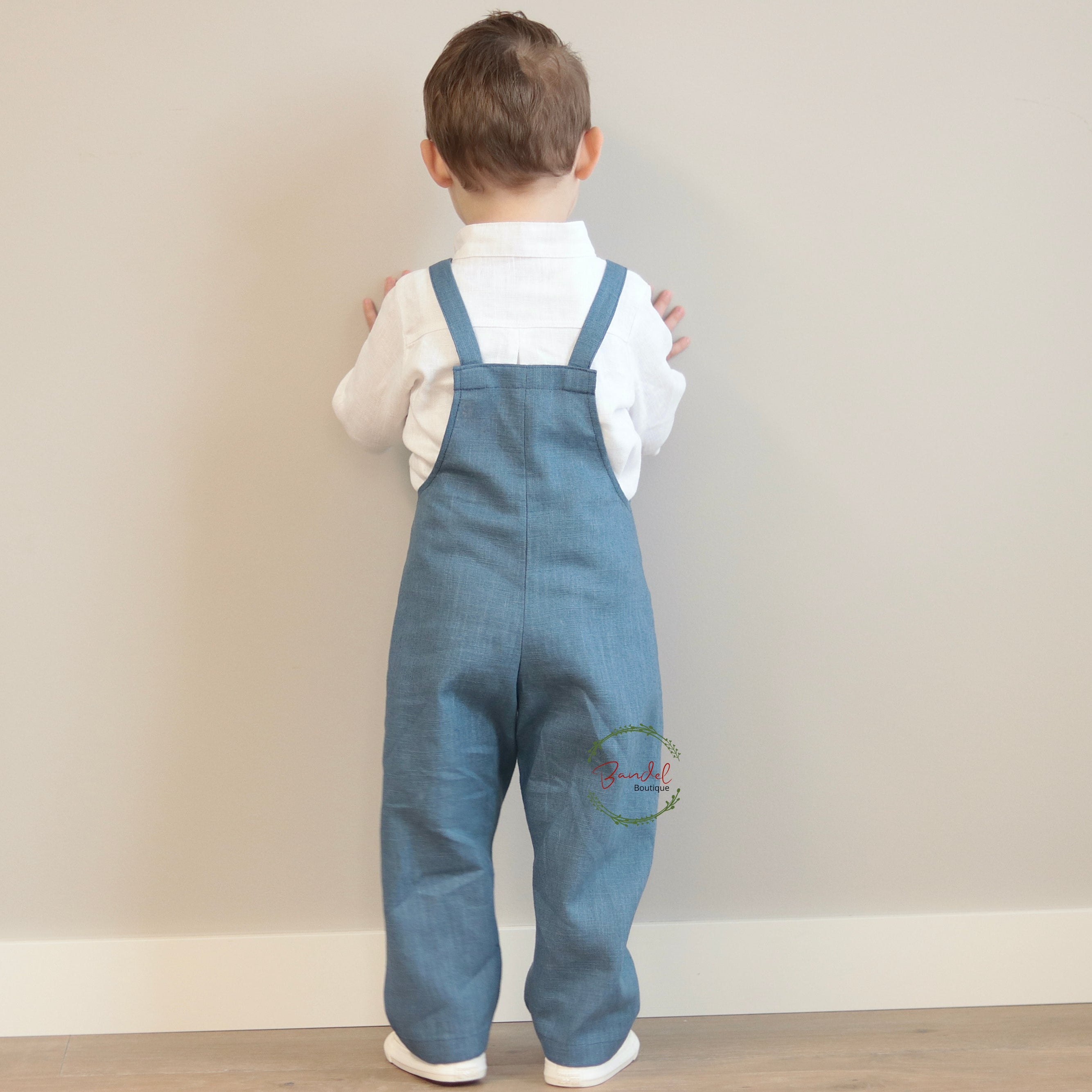 Child wearing blue denim overalls and a white shirt against a plain background