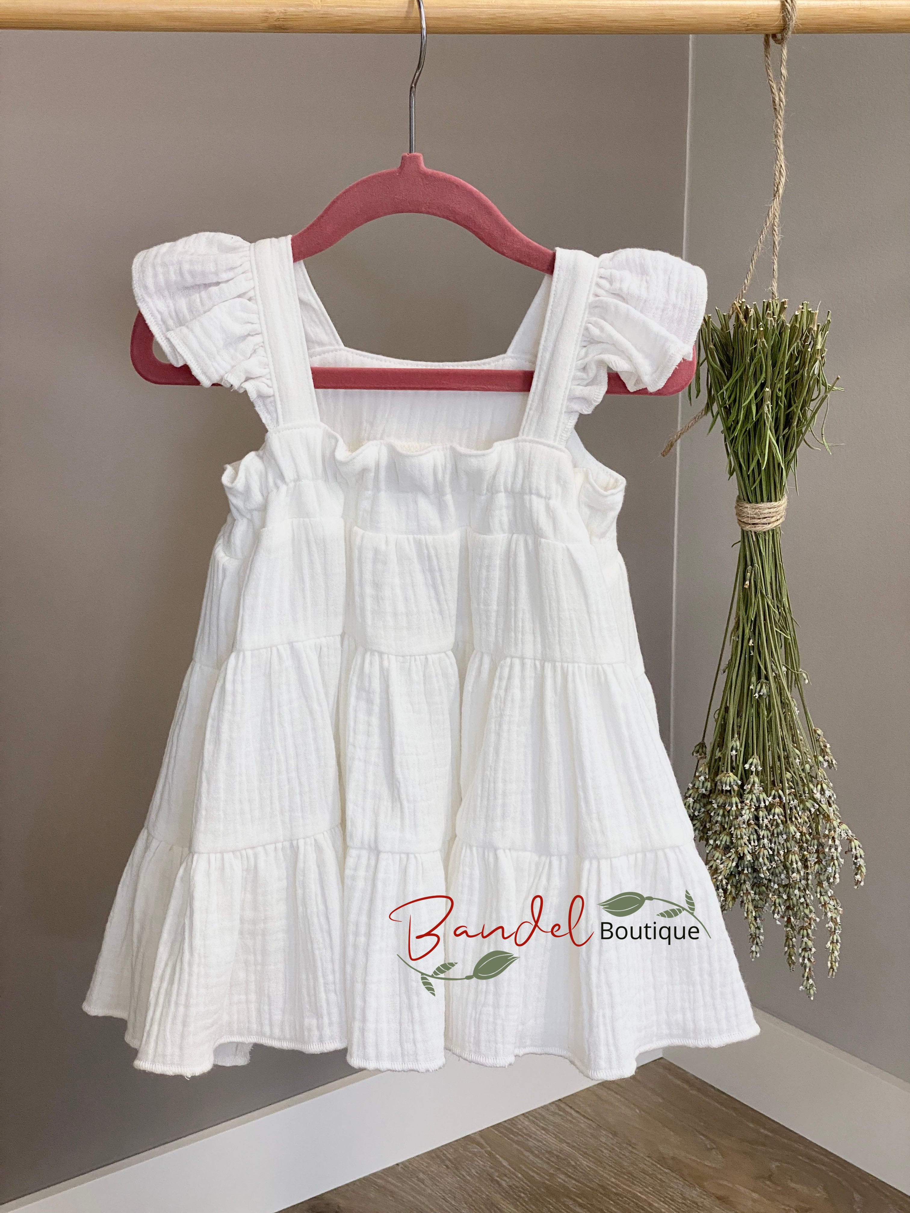 White dress with ruffled sleeves and bottom hanging on a hanger against a neutral background.