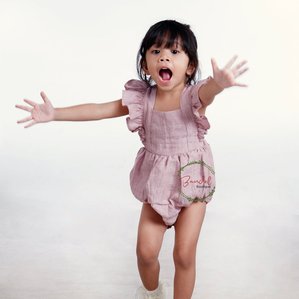 old- rose vintage-inspired Linen Bubble Romper is handmade with care in the Netherlands, making it a unique piece for your baby's wardrobe. This playsuit features sleeve ruffles, elastic at the leg for a comfortable fit, adjustable button straps with two buttonholes, and snaps at the crotch for easy diaper changes.