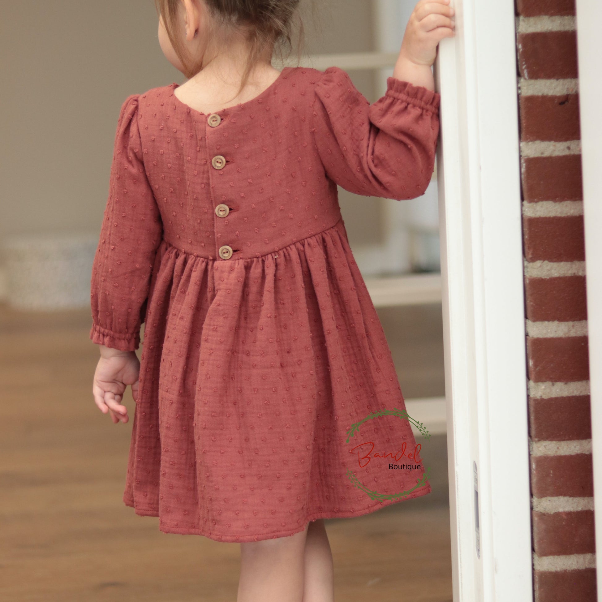 Child wearing a red dress with buttons, standing indoors.