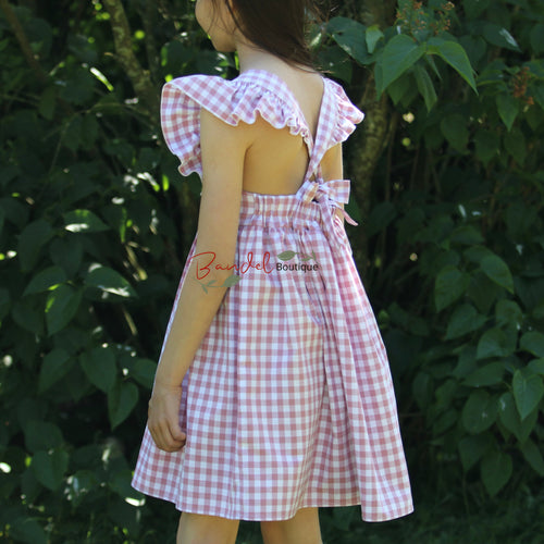 Person wearing a pink and white checkered dress with ruffled sleeves in a forest setting