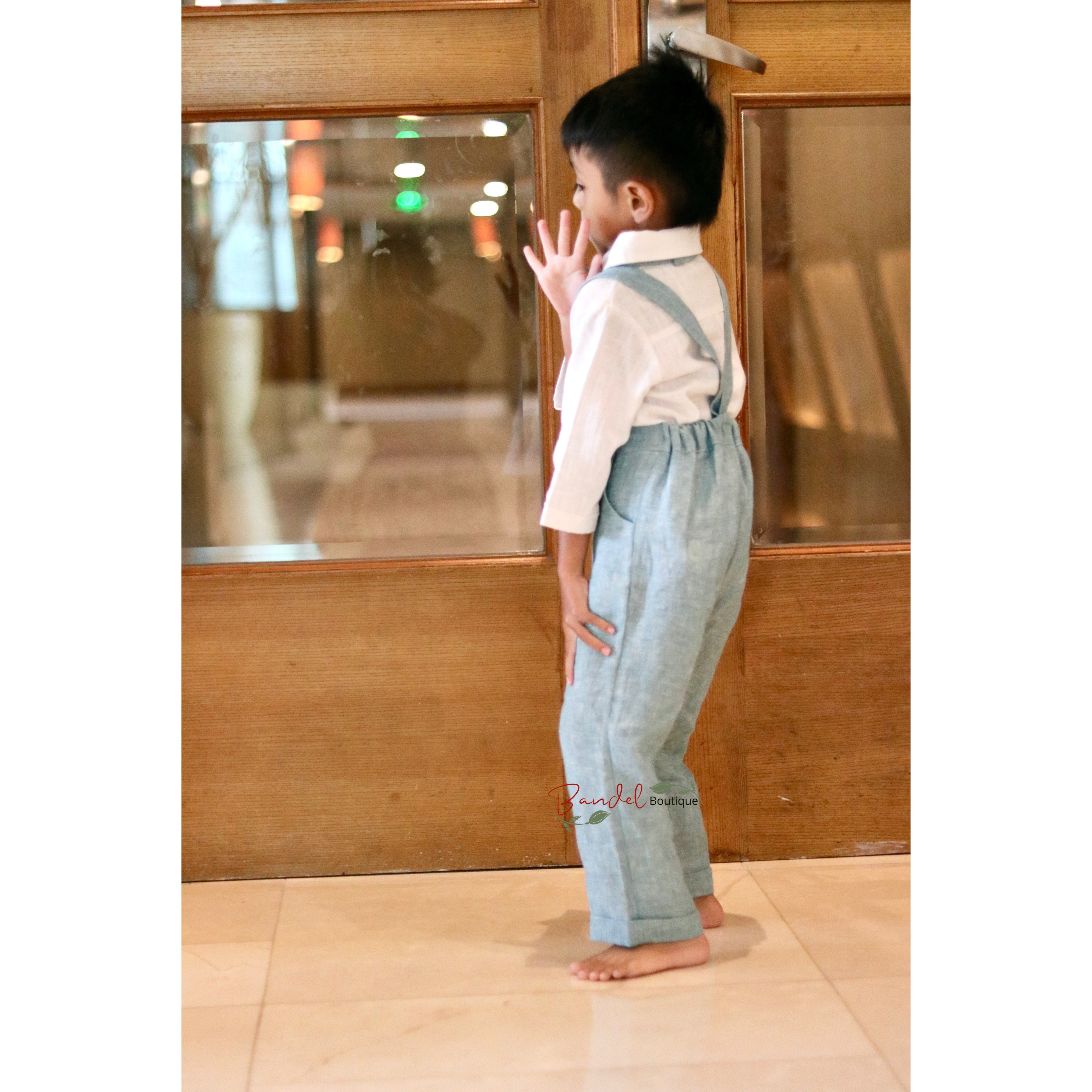 Child wearing light blue overalls standing in front of a wooden door.