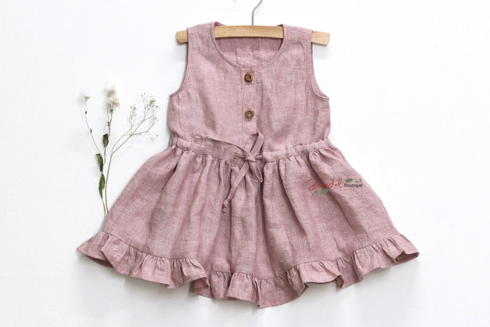 Pink dress with buttons on a wooden hanger against a white background