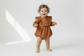 Child wearing a brown ruffled romper on a white background