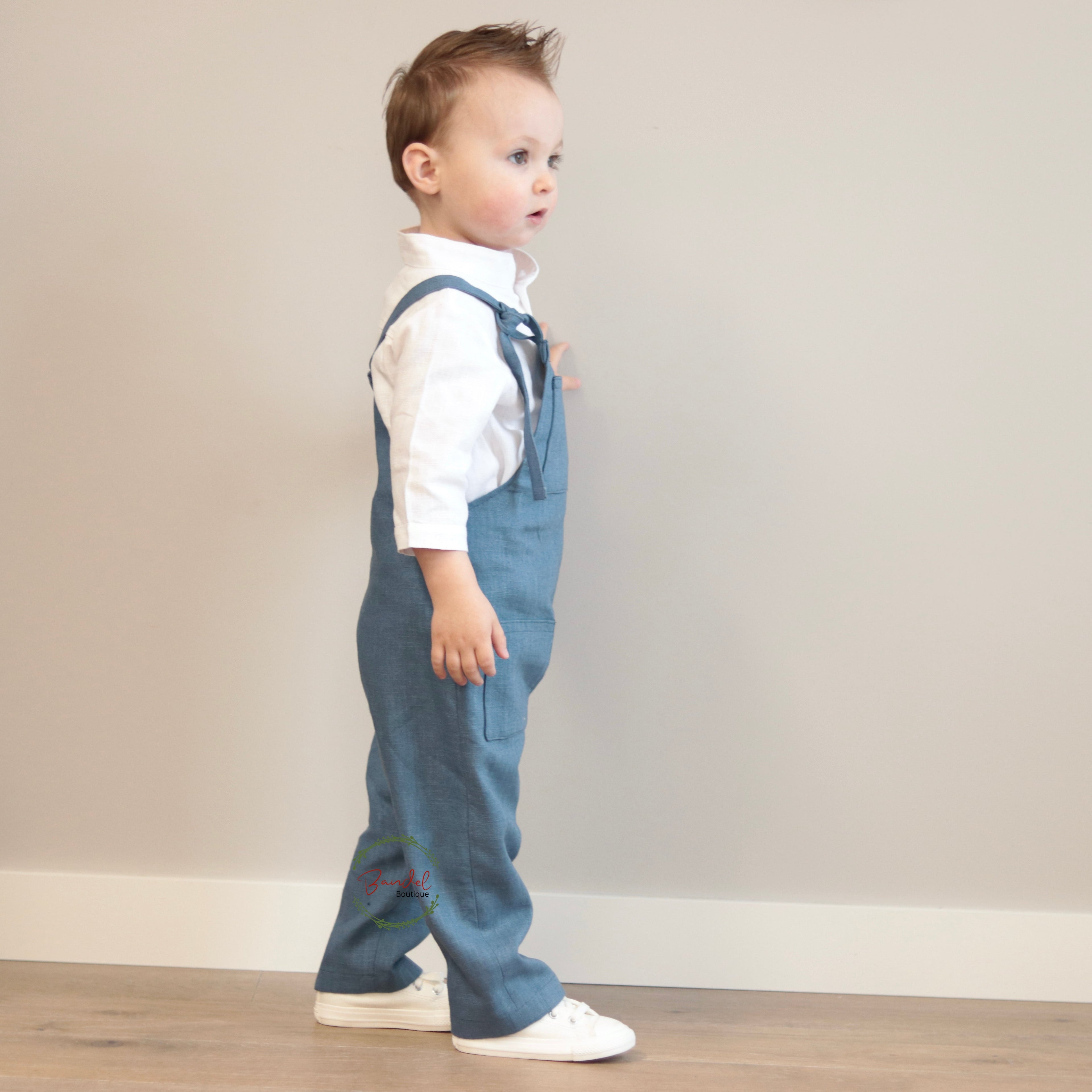 Child wearing blue denim overalls and a white shirt against a plain wall.