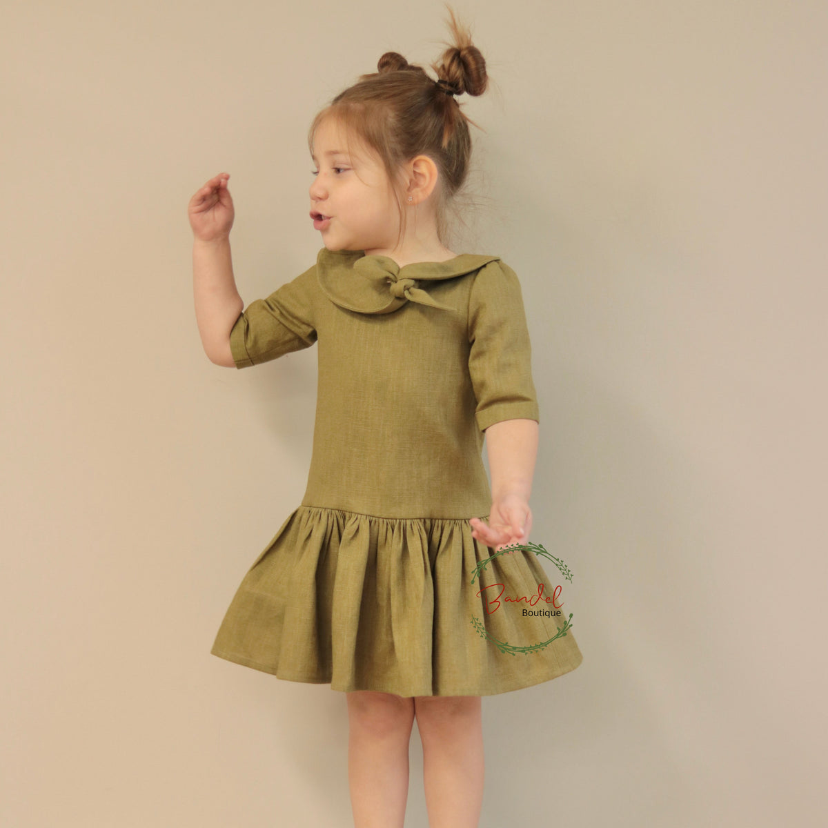 Young girl wearing a green dress with a bow collar against a beige background