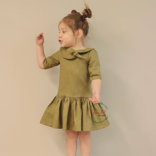 Young girl wearing a green dress with a bow collar against a beige background