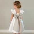 Children's dress with a large bow on a hanger against a beige background