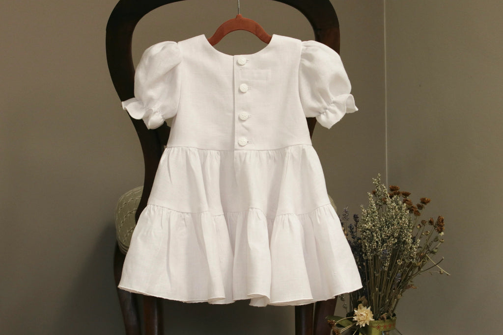 White dress with puffed sleeves on a wooden chair against a neutral background