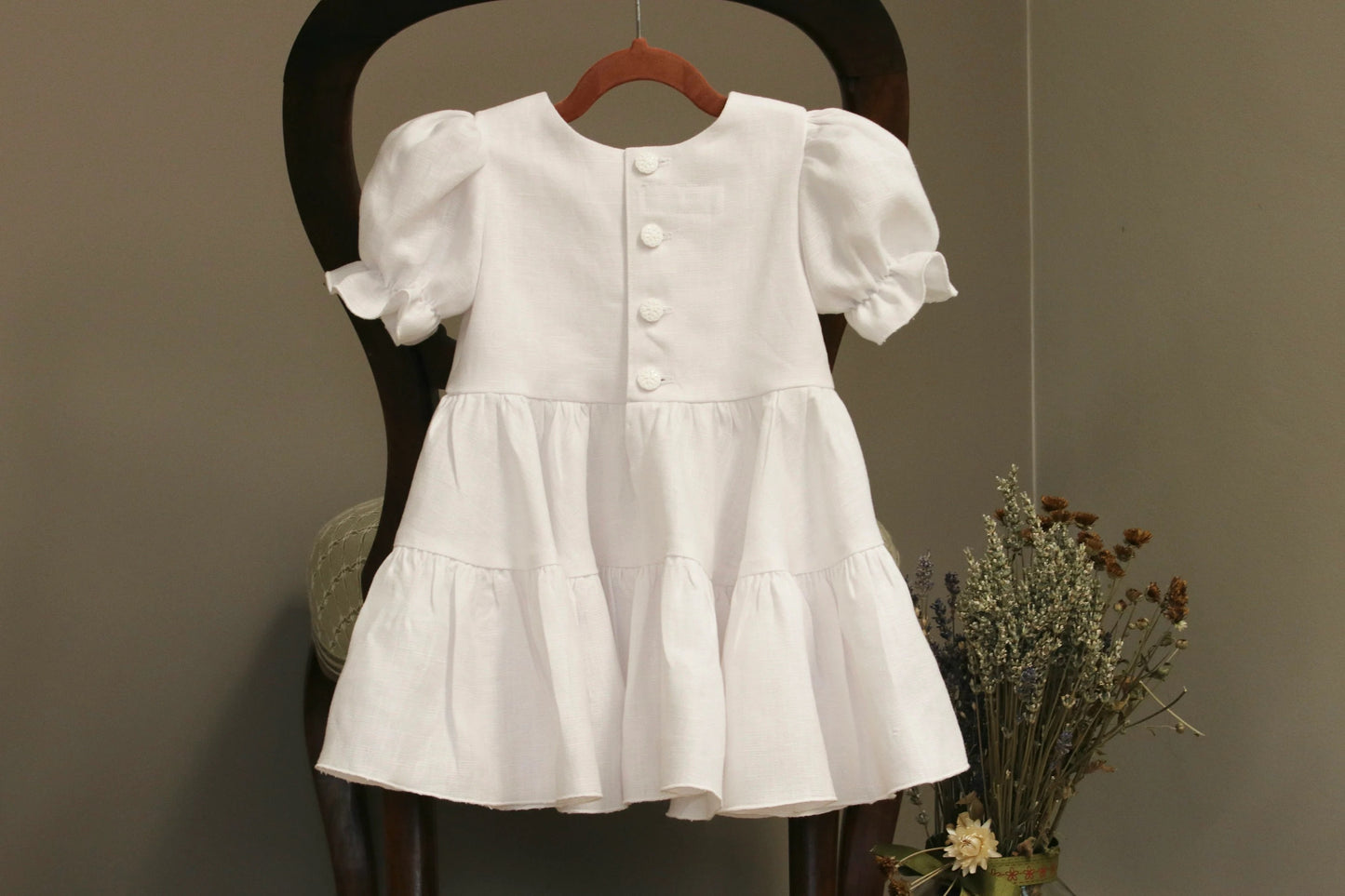 White dress with puffed sleeves on a wooden chair against a neutral background