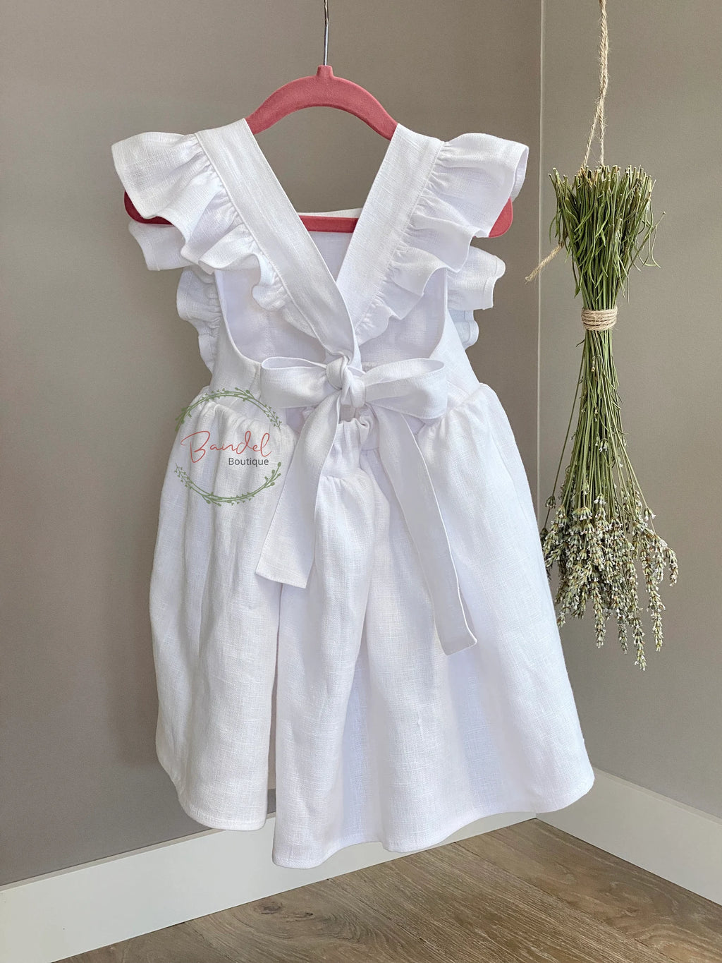 White dress with ruffled details on a hanger against a plain wall.