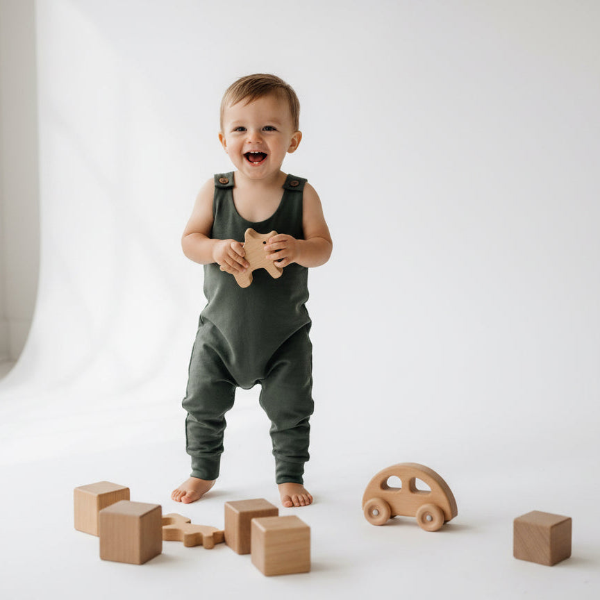 Child in green overalls playing with wooden toys on a white floor.